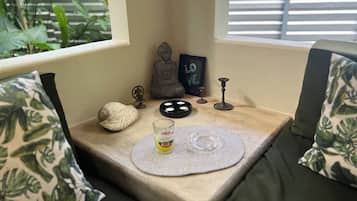 A cozy corner with a cushioned bench, a small table with a mat, a Buddha statue, a framed sign, a candle holder, and a decorative shell.