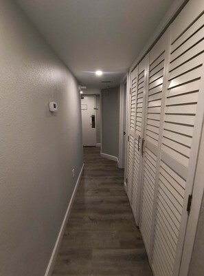A narrow hallway with a wooden floor, white walls, and a white door at the end. - Relaxing 3 BR Condo Modern Decor with Pool Access (Myrtle Beach)