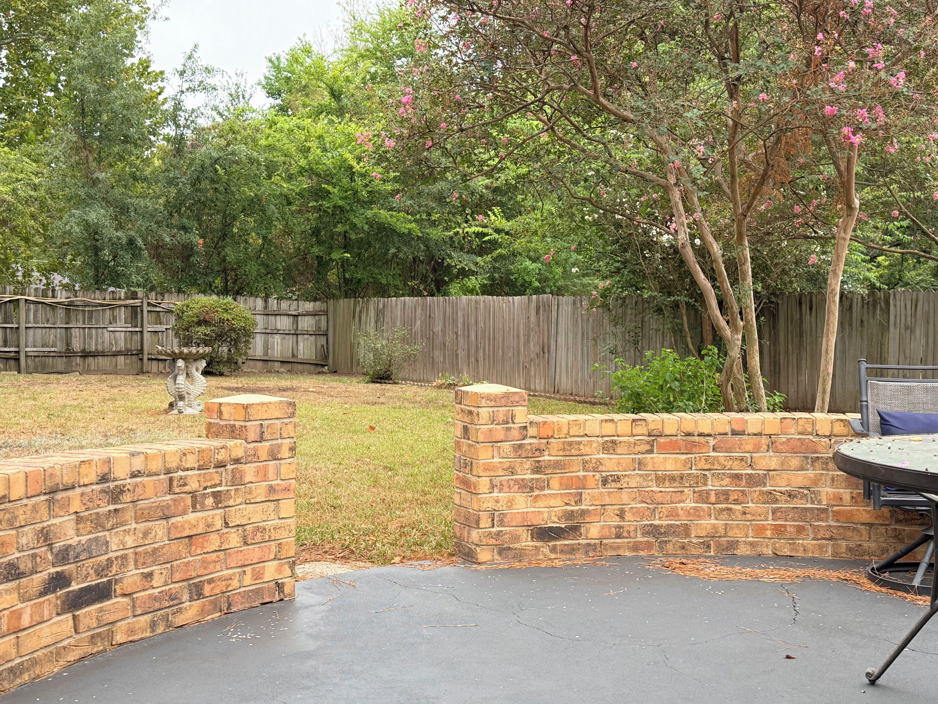 A backyard with a brick patio, a wooden fence, and a tree with pink flowers.