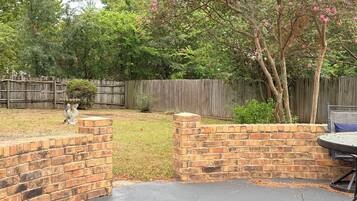A backyard with a brick patio, a wooden fence, and a tree with pink flowers.