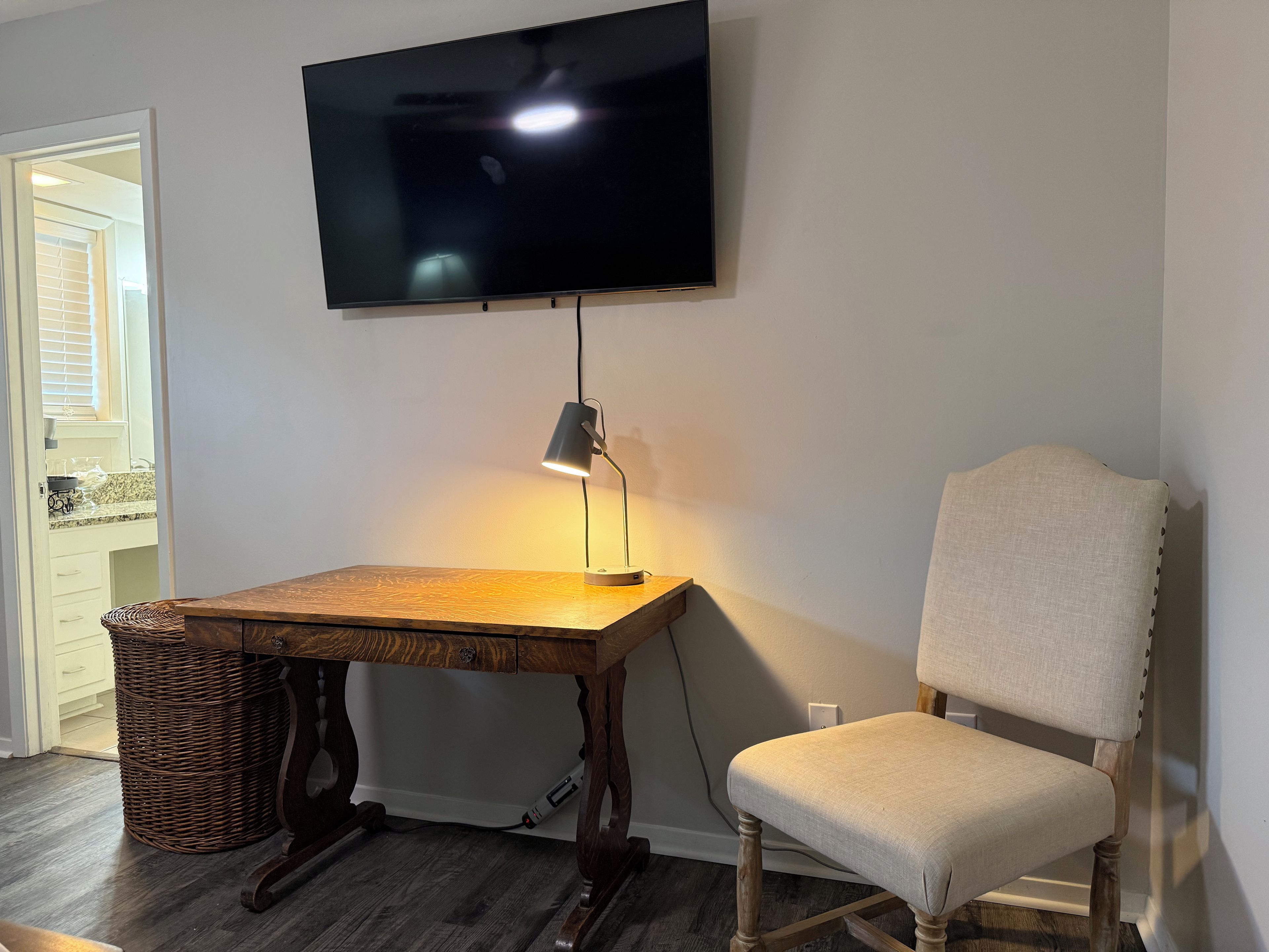 Une pièce avec une table en bois, une chaise, un téléviseur fixé au mur et une lampe sur la table.