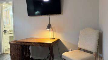 Une pièce avec une table en bois, une chaise, un téléviseur fixé au mur et une lampe sur la table.