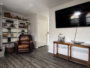 A living room with a leather armchair, a wooden coffee table, a bookshelf, and a mounted flat-screen TV. - Wonderful 3-bedroom townhome with AC in charming Longview (Longview)