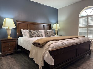 A bedroom with a large bed, two bedside tables, a nightstand, and a window with blinds. - Wonderful 3-bedroom townhome with AC in charming Longview (Longview)