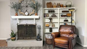 A room with a fireplace, a leather armchair, and a bookshelf with various decorative items.