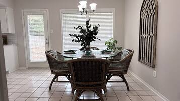 A dining area with a round table, four wicker chairs, a chandelier, and a decorative wall piece.