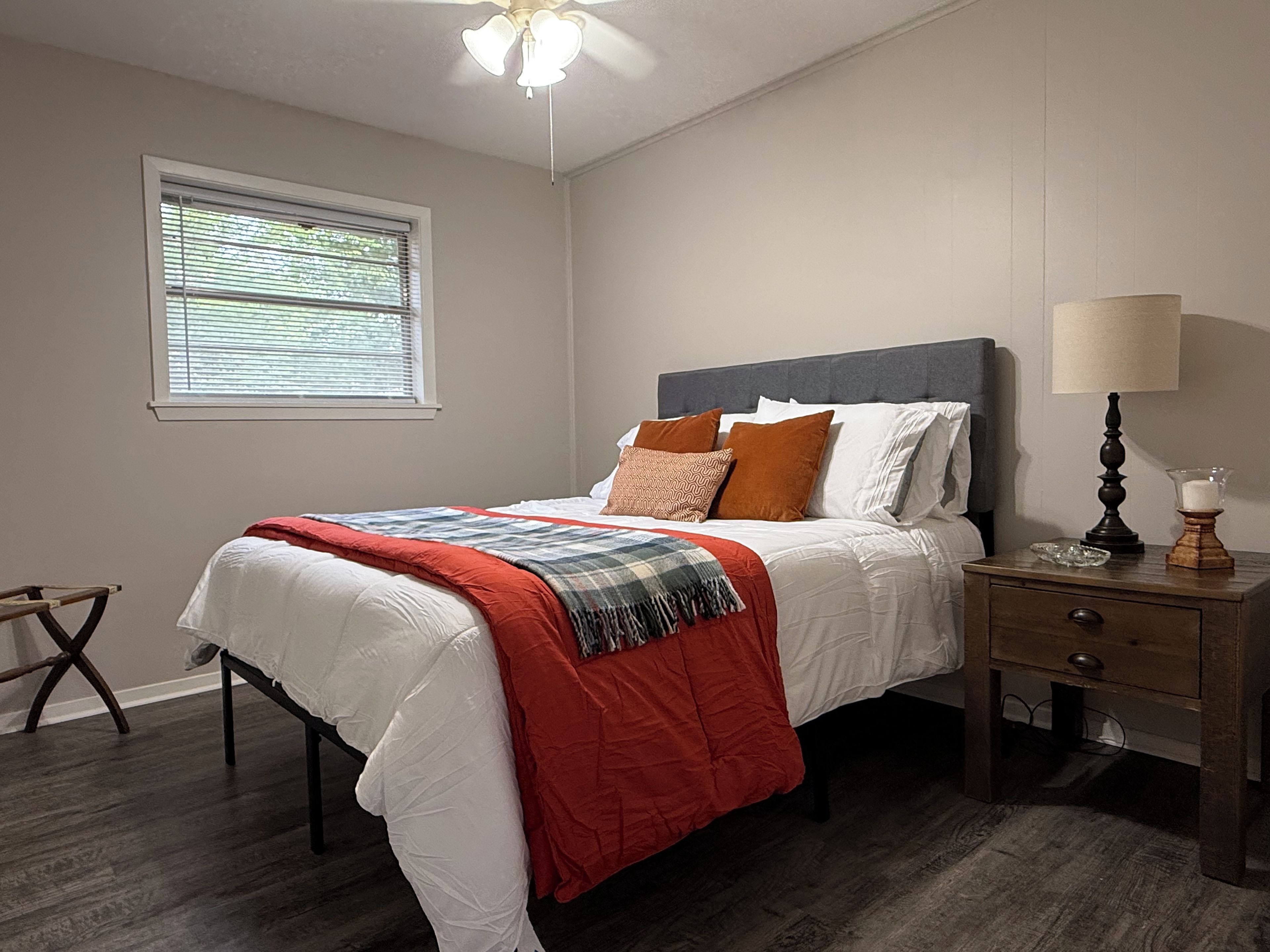 Un dormitorio con cama, mesita de noche, lámpara y ventana.