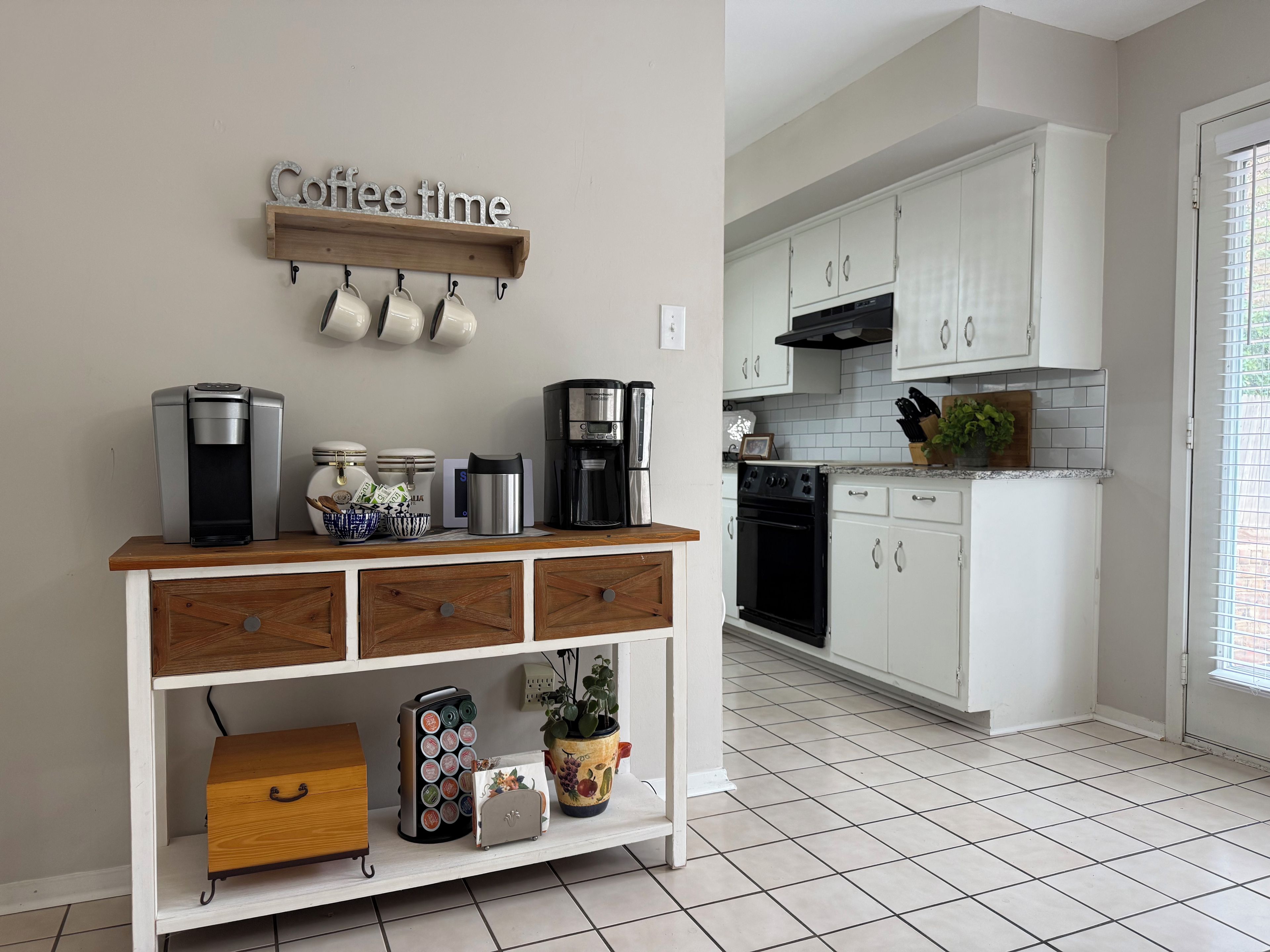 Una cocina con armarios blancos, una estación de café y piso de baldosas.