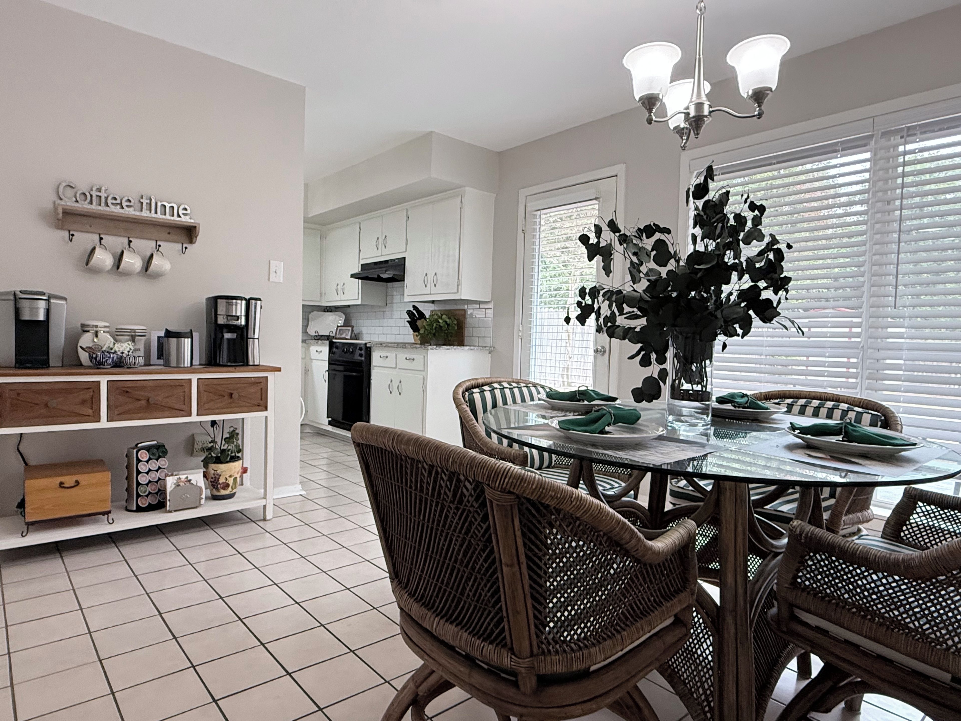 A modern kitchen with white cabinetry, a dining table with wicker chairs, and a coffee sign on the wall.