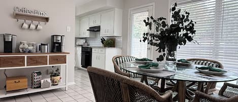 A modern kitchen with white cabinetry, a dining table with wicker chairs, and a coffee sign on the wall.