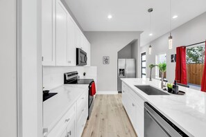 A modern kitchen with white cabinetry, a black stove, and a stainless steel refrigerator. - Cozy 3BR - Walk to Fair Park - Pool Table, Fire Pit (Dallas)