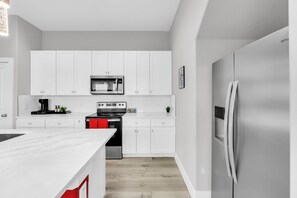 A modern kitchen with white cabinetry, a stainless steel refrigerator, and a built-in oven. - Cozy 3BR - Walk to Fair Park - Pool Table, Fire Pit (Dallas)