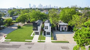 A residential area with modern houses, a well-maintained lawn, and a clear view of a city skyline in the background. - Cozy 3BR - Walk to Fair Park - Pool Table, Fire Pit (Dallas)