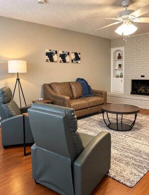 A living room with a sofa, two armchairs, a coffee table, a floor lamp, and a fireplace. - The Stillwater Haven (Stillwater)