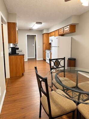 A modern kitchen with wooden cabinets, a refrigerator, and a dining area with a glass table and chairs. - The Stillwater Haven (Stillwater)