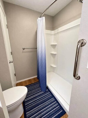 A bathroom with a white toilet, a shower with a blue gradient curtain, and a white bathtub. - The Stillwater Haven (Stillwater)