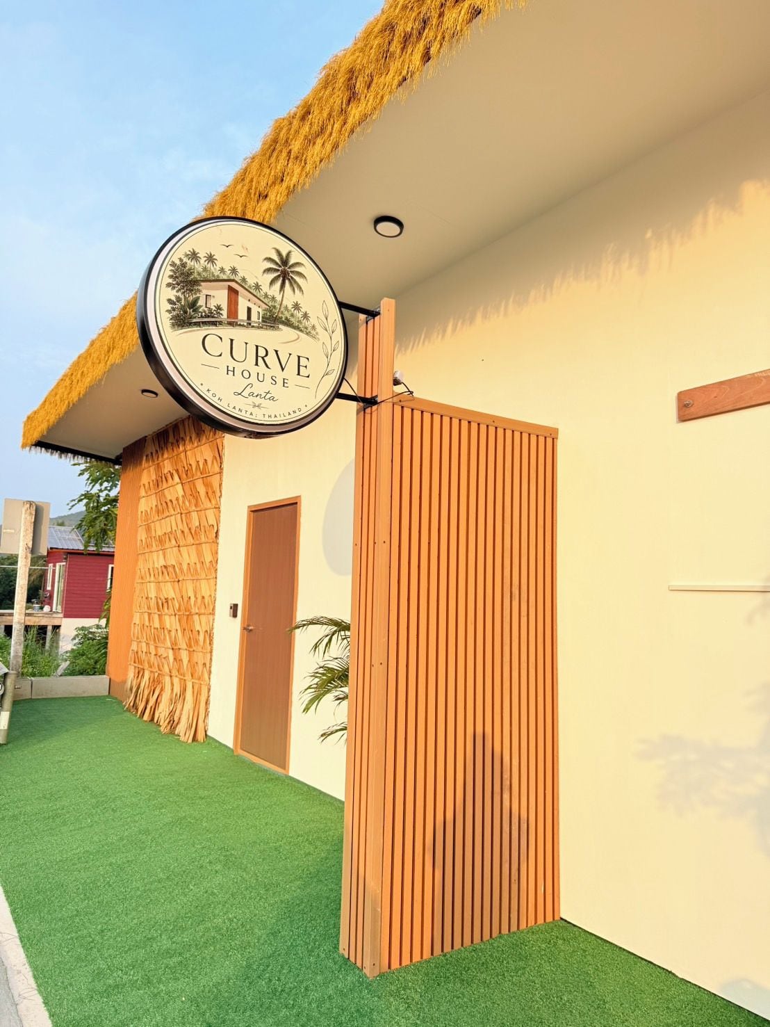 Un letrero de hotel con temática tropical, techo de paja y puerta de madera.