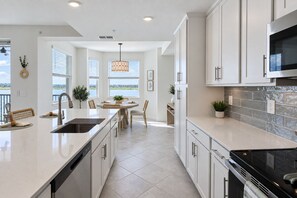 A modern kitchen with a central island, white cabinetry, and a view to the outdoors. - Stunning Lakefront Calusa Country Club Condo - A Slice Of Paradise (Bradenton)
