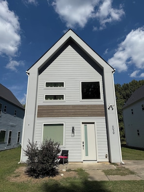 A two-story building with a gabled roof, a garage door, and a small porch with a chair. - Spacious 4-bedroom house across from 73 acre park near Uptown Charlotte (Charlotte)