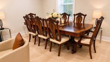 A dining room with a wooden table surrounded by chairs, a vase with flowers, and a window with blinds.