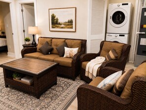A living room with a sofa, armchair, coffee table, and a washing machine in the background. - Modern 6BR Home Walk to Metro, Navy Yard & Wharf (Washington)