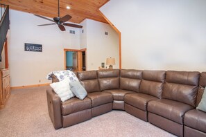 A spacious living room with a brown leather sectional sofa, a ceiling fan, and a welcome sign on the wall. - The Cabin on Pine Creek (Cammal)