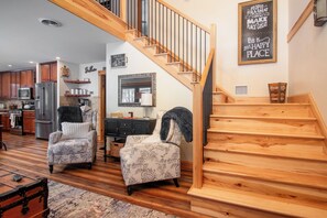 A home interior with a wooden staircase, a kitchen with a refrigerator, and two patterned armchairs. - The Cabin on Pine Creek (Cammal)