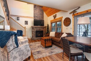 A cozy living room with a fireplace, a wooden staircase, and a dining area with a large wooden table. - The Cabin on Pine Creek (Cammal)