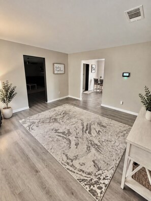 A spacious living area with hardwood flooring, a large patterned rug, and a dining area with a table and chairs.