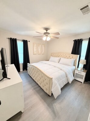 A bedroom with a bed, a desk, a ceiling fan, and artwork on the wall.