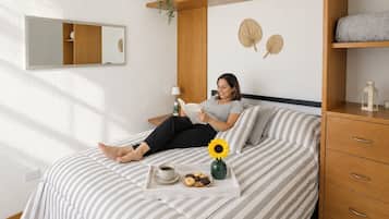 A bedroom with a bed, a bedside table with a lamp, a nightstand, a mirror, and a shelf with decorative items.