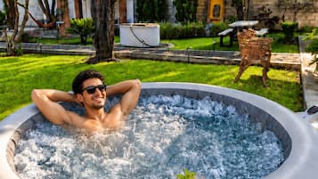 A person relaxing in a hot tub with a drink on a tray.