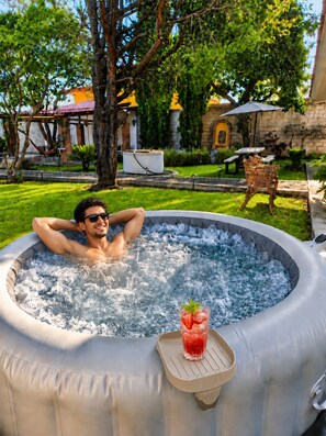 A person relaxing in a hot tub with a drink on a tray. - Quinta San Gabriel | Cabin with Jacuzzi, Garden, Fire Pit, and Peace (Atlixco)
