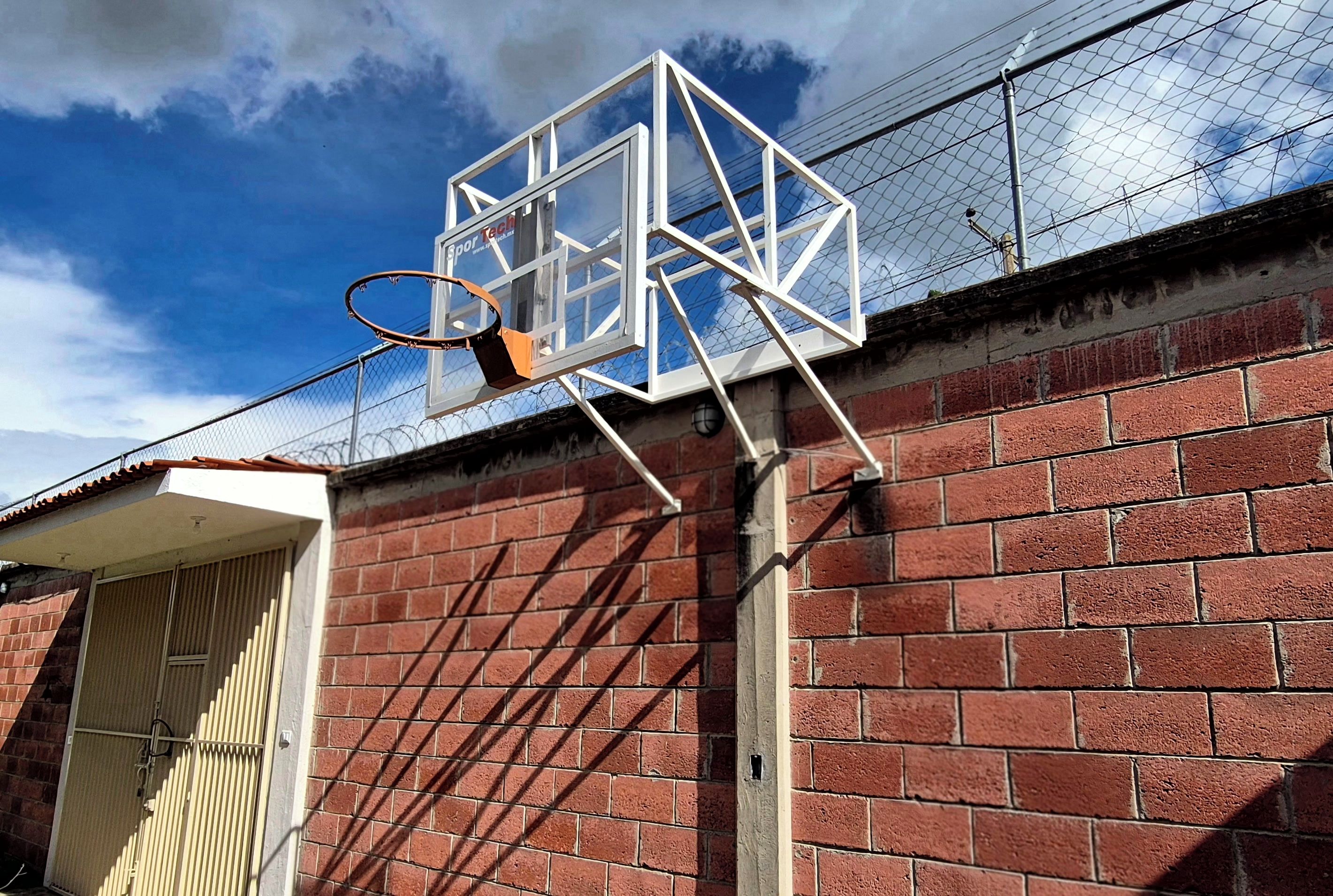A basketball hoop attached to a brick wall with a metal frame and a chain.