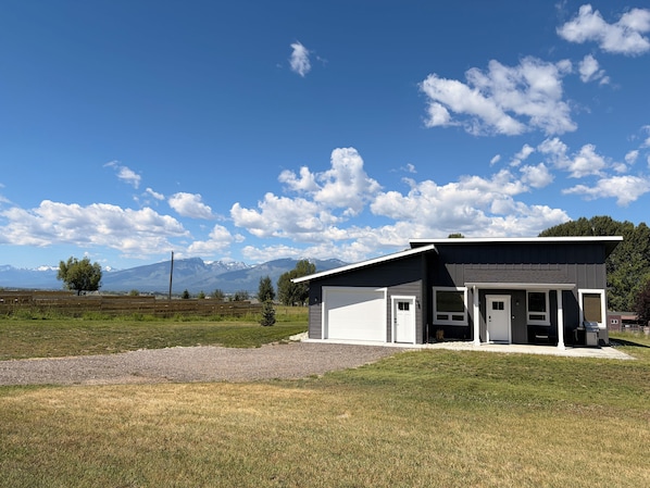 Ein modernes Gebäude mit Garage, überdachter Veranda und Blick auf Berge im Hintergrund.