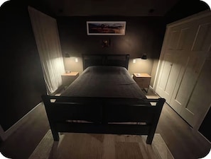 Ein Schlafzimmer mit einem Bett, zwei Nachttischlampen, einem Bild an der Wand und einer Tür.