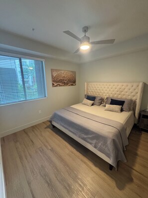 Ein Schlafzimmer mit einem Bett, einem Deckenventilator, einem Fenster mit Jalousien und einem Wandbild.