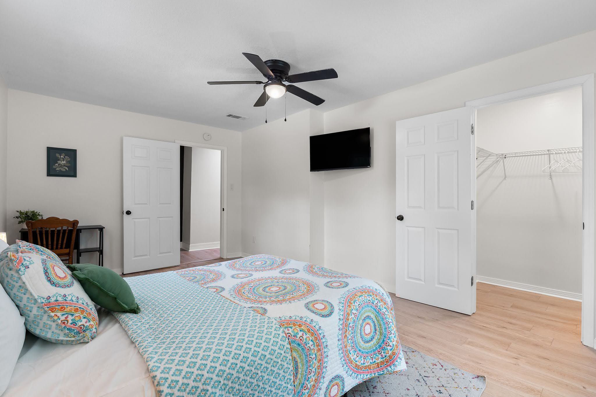 A bedroom with a bed, a ceiling fan, a TV, and a door leading to another room.