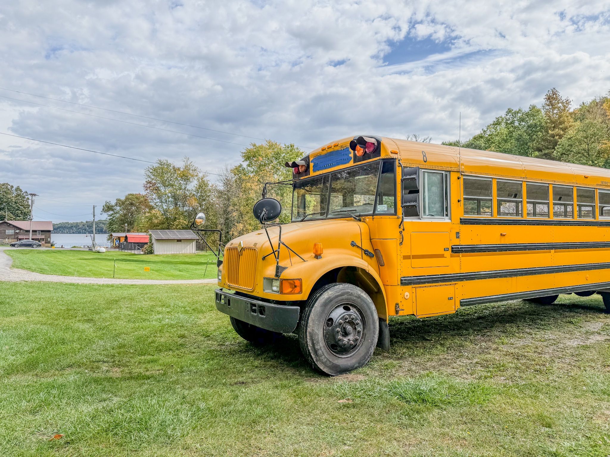 A yellow school bus parked on a grassy area with a lake and buildings in the background.