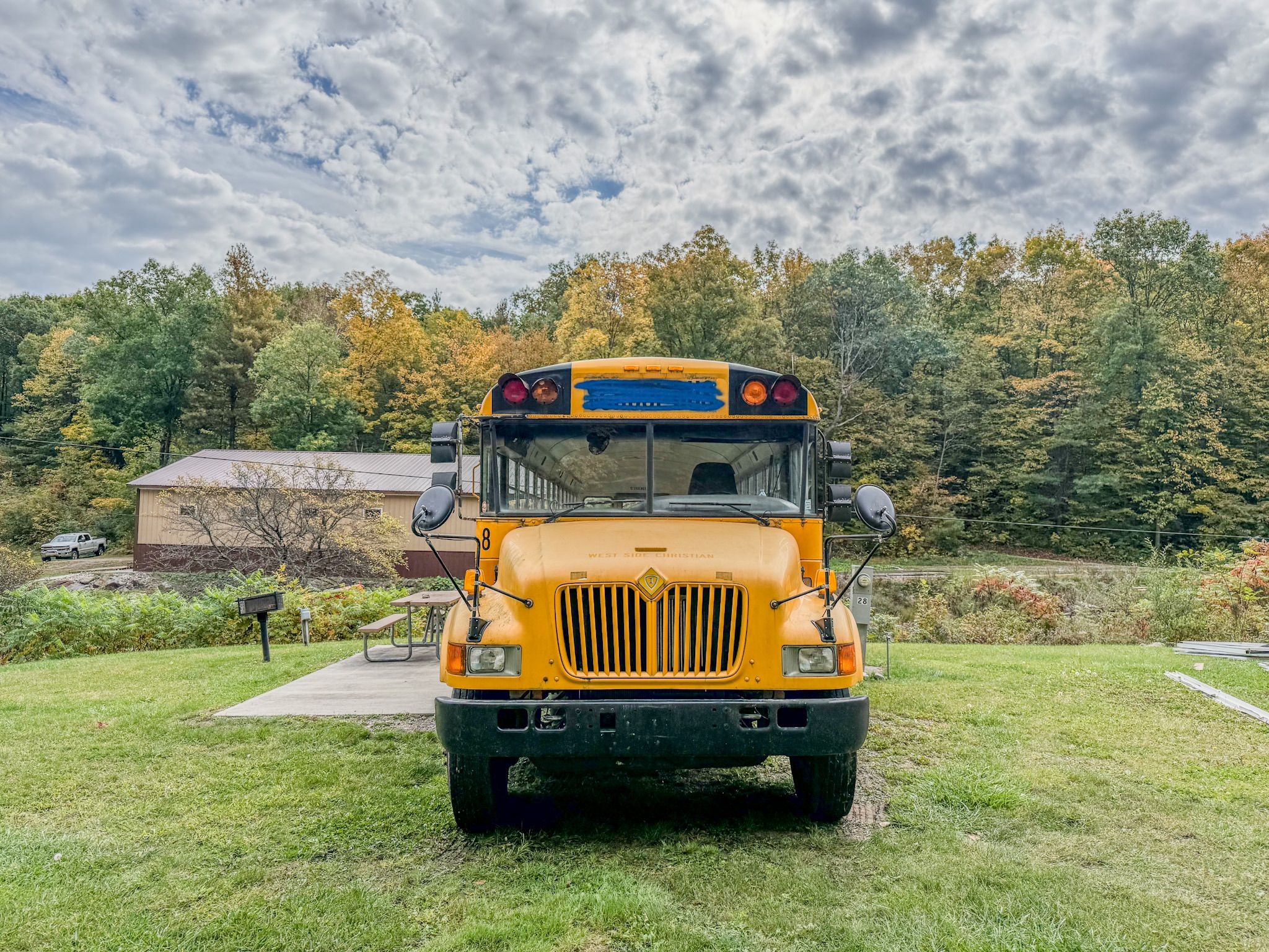 A yellow school bus parked on grass with trees and a building in the background.