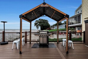 Une terrasse en bois avec un barbecue et un espace salon donnant sur une plage.