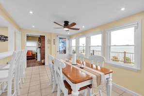A dining area with a wooden table and white chairs, a ceiling fan, and large windows with a view of the sea. - Peaceful Lake Ontario waterfront & sunsets (Lyndonville)