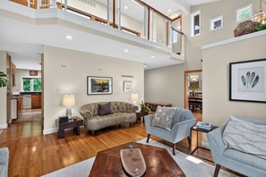 Un vaste espace de vie doté d’un plafond haut, d’un plancher en bois franc et d’une variété de sièges, notamment un canapé et des fauteuils.