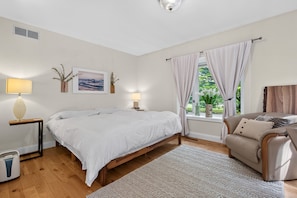 Ein Schlafzimmer mit Bett, Nachttischlampen, einem Fenster mit Vorhängen, einem Sofa und einer Heizung.