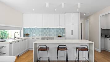 A modern kitchen with white cabinetry, a central island with bar stools, and a backsplash with blue tiles.