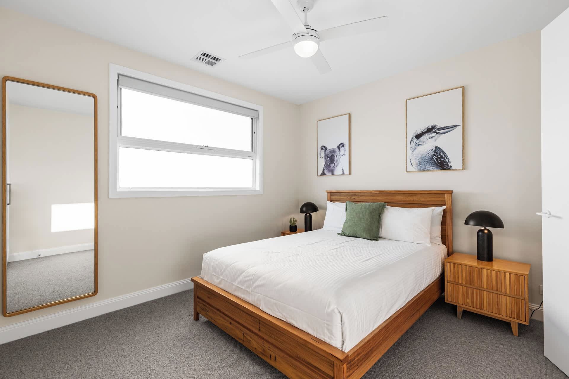 A bedroom with a bed, a window, a ceiling fan, and two wall-mounted lamps.