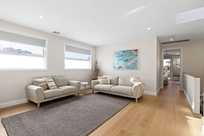 A spacious living room with a large window, a beige sofa, a small round table, and a colorful abstract painting on the wall. - Heated pool, Rosewood Retreat (Rosebud)