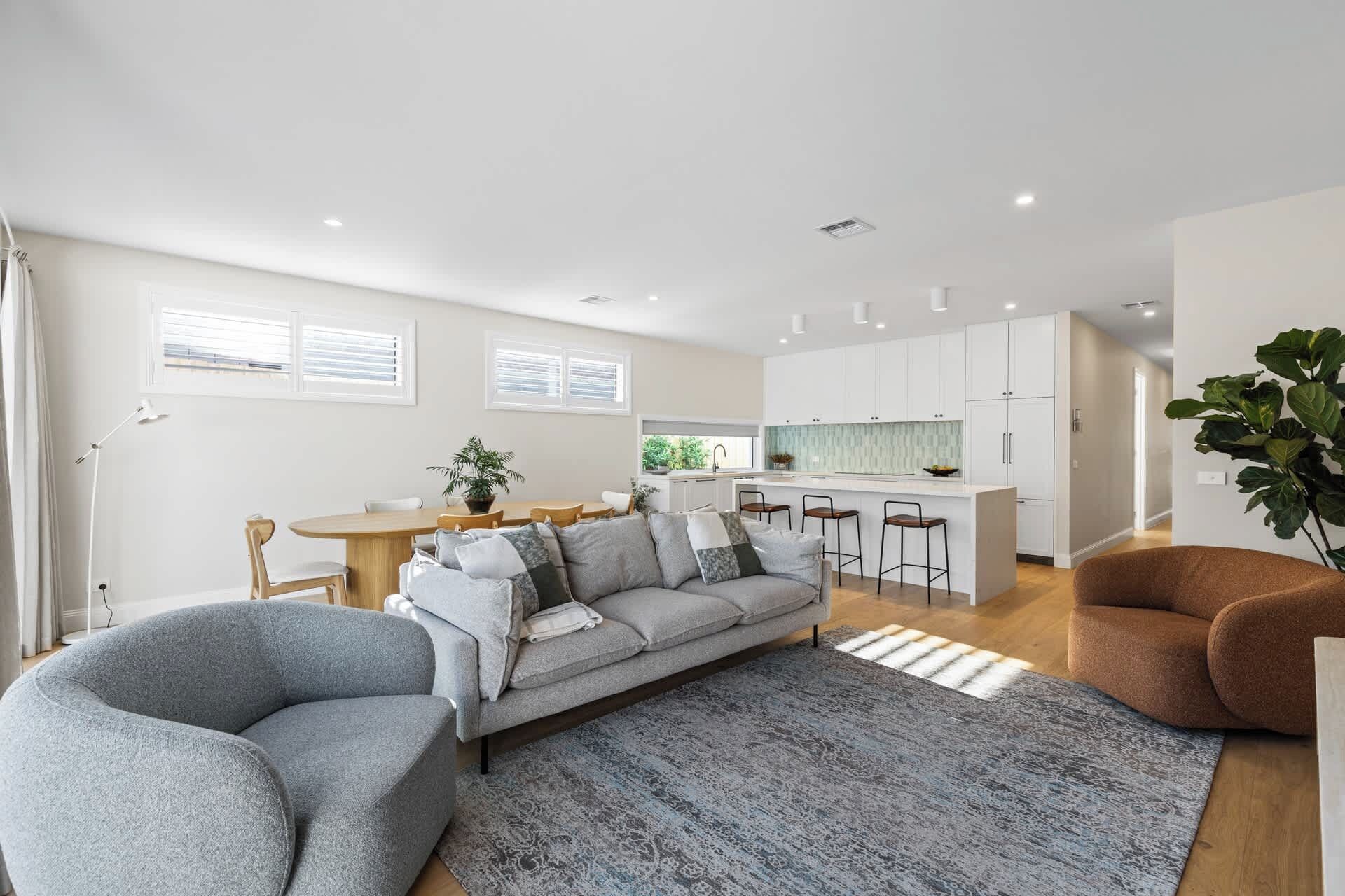 A modern living room with a sofa, chairs, a rug, and a kitchen in the background.