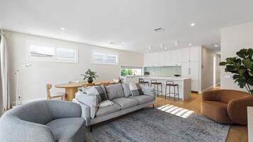 A modern living room with a sofa, chairs, a rug, and a kitchen in the background.