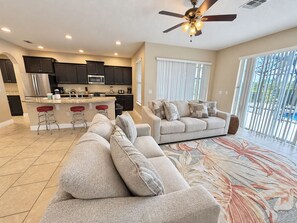 A modern kitchen with dark cabinets, a central island with stools, and a dining area with a sofa and a coffee table. - Family-Friendly Luxury Villa | Sleeps 14 | Private Pool, Game Room & More! (Davenport)